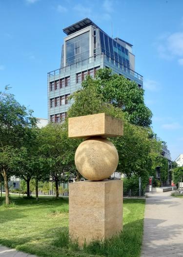 Foto, Skulptur, Rasen, Hochhaus im Hintergrund, blauer Himmel
