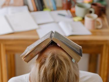 Studentische Verzweiflung: Studierende mit Buch über dem Gesicht wie ein Hausdach