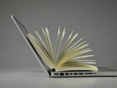Offener Laptop mit aufgeblättertem Buch