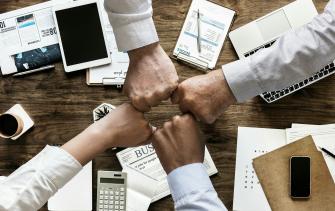 Vier Hände kommen am Arbeitsplatz zusammen 